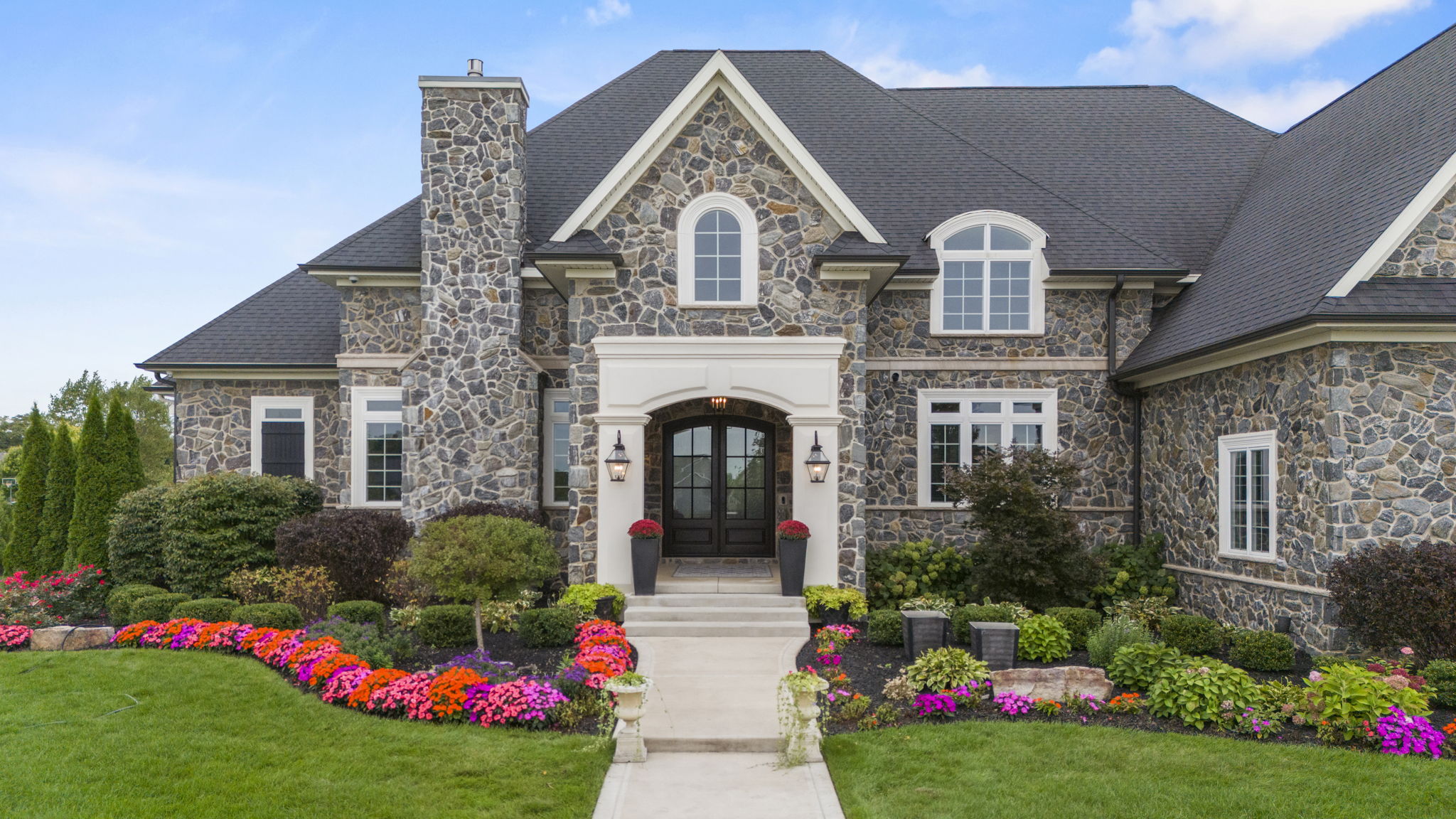 Front of a stone house with flowers all around the front in various colors