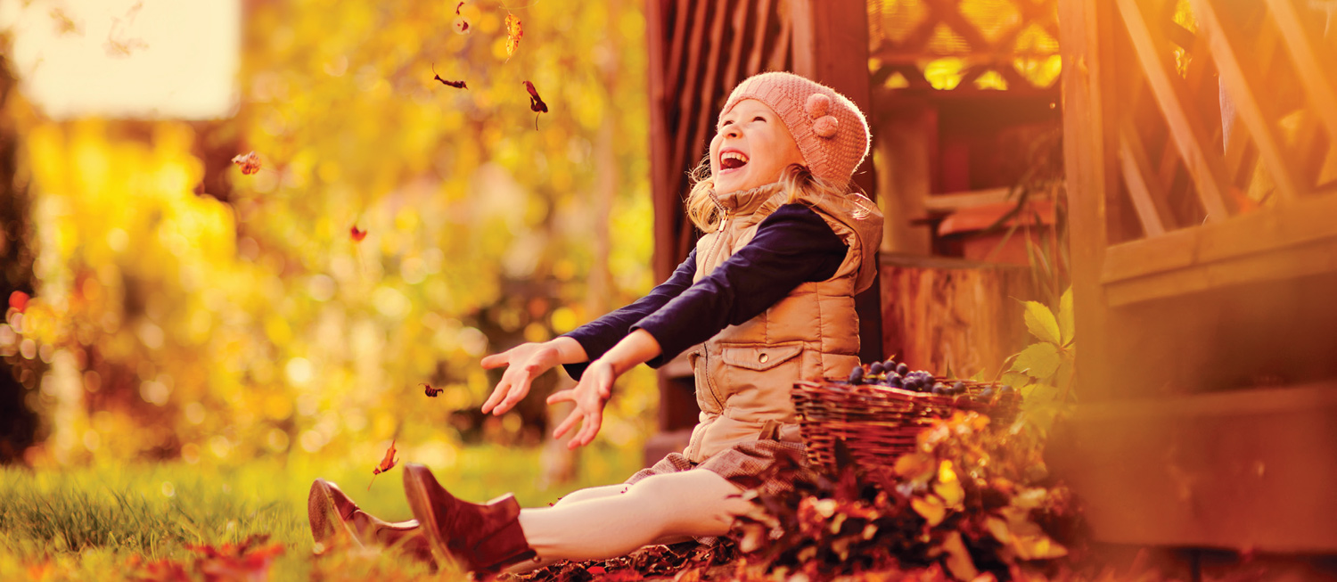 Child throwing leaves and smiling, enjoying the fall season